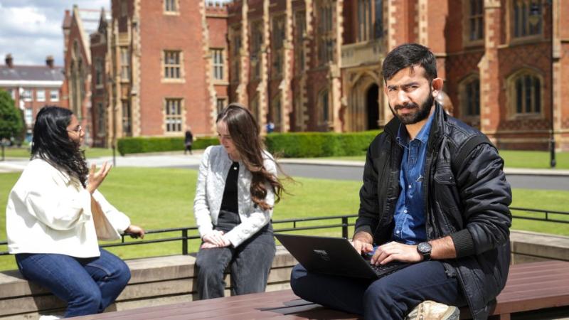male student sitting with a laptop in front of the main Queen